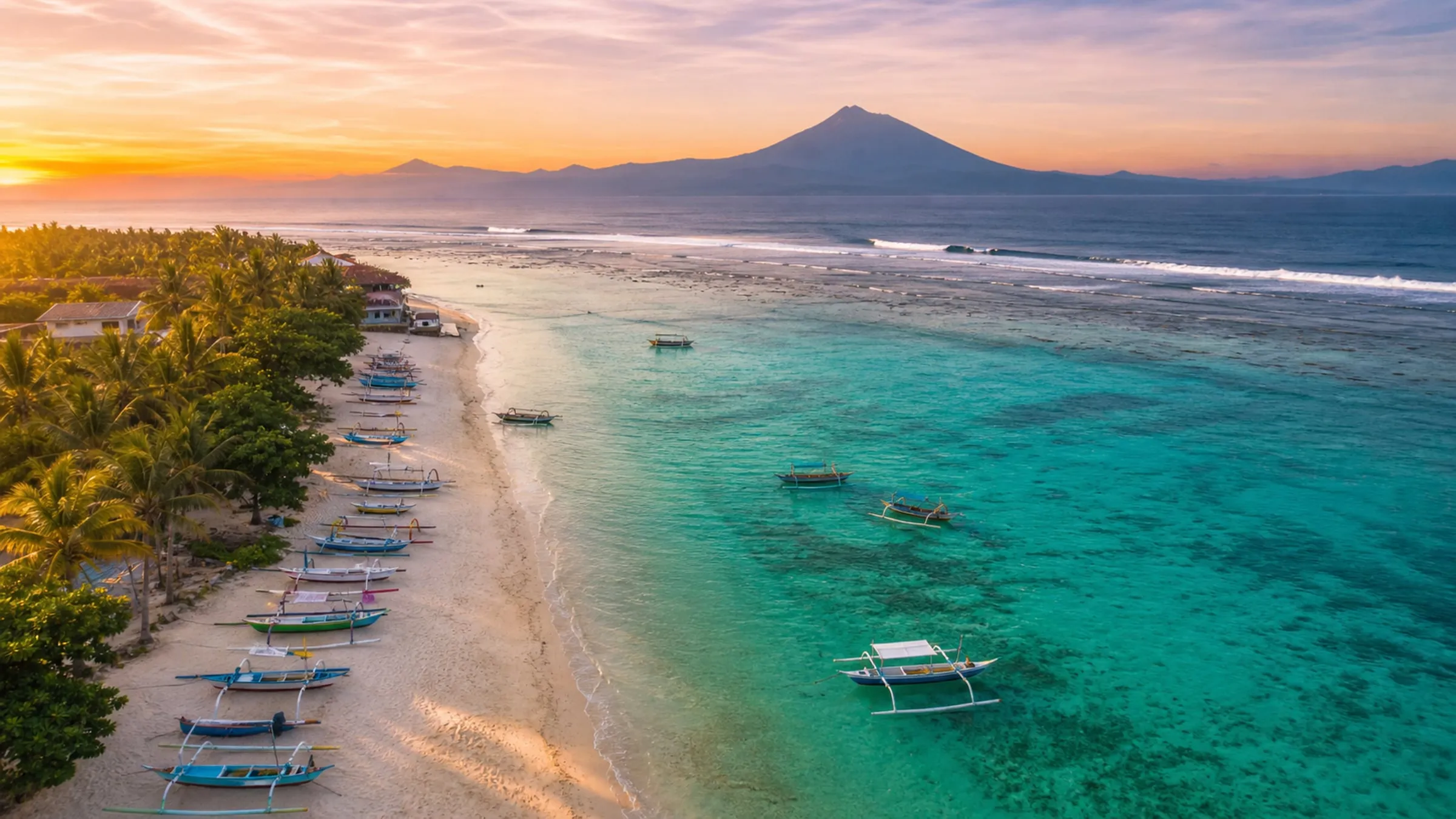 Surfer riding a wave at Nusa Lembongan with jukung boats and Mount Agung behind