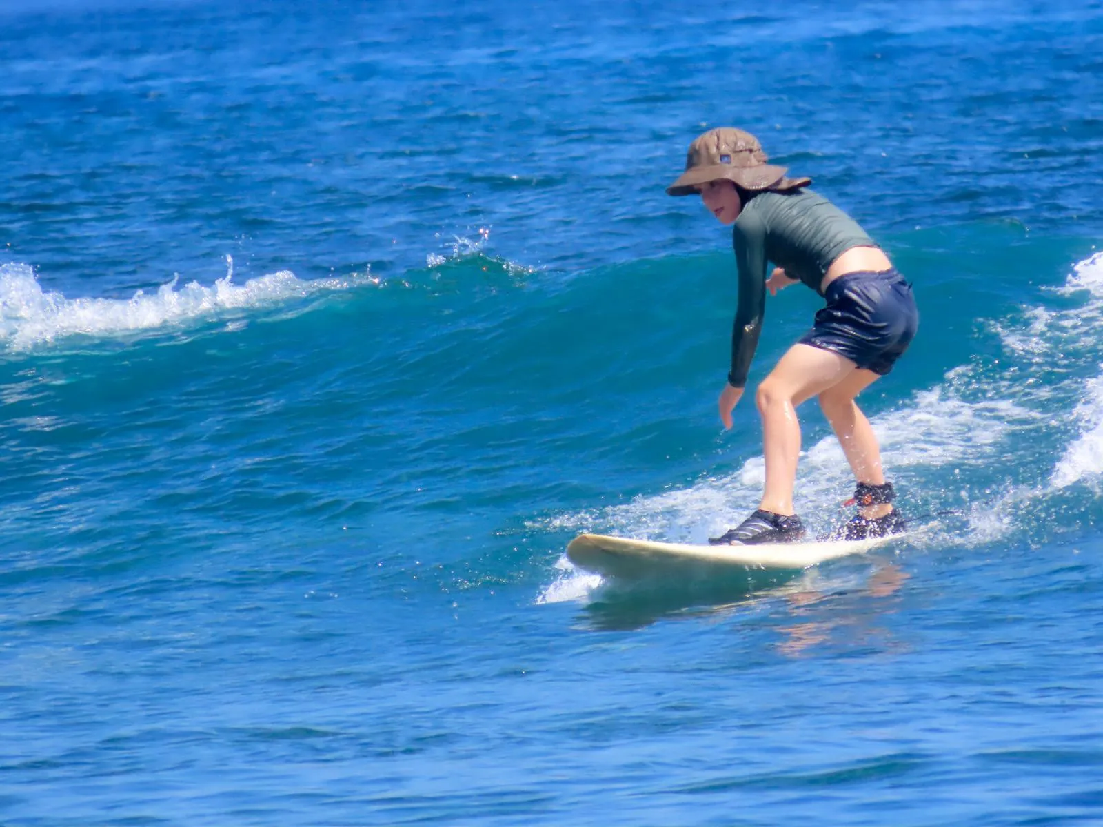 A first-time surfer riding a longboard across a clean wave at Nusa Lembongan