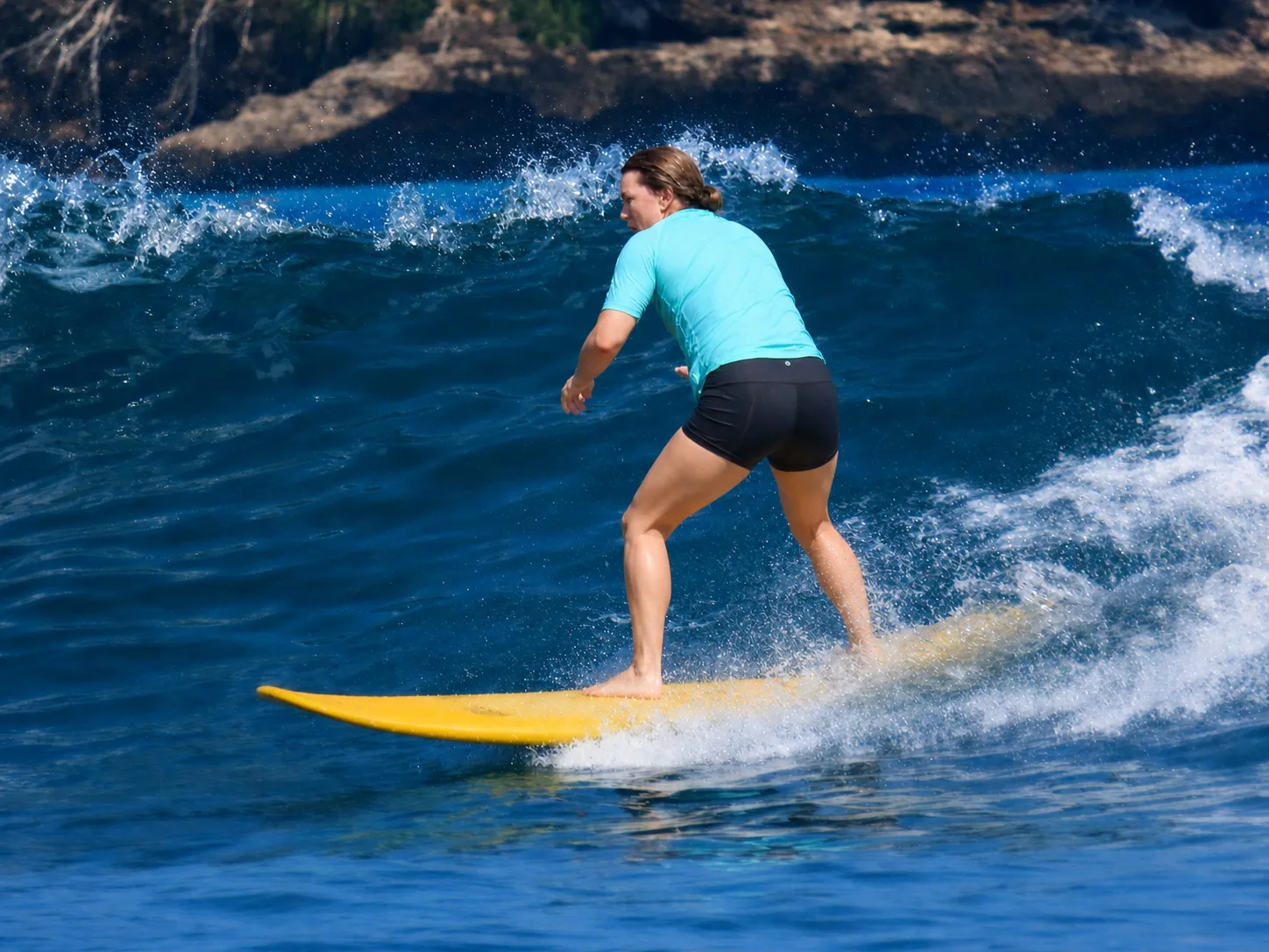 An adult beginner riding a wave on a yellow longboard at Nusa Lembongan