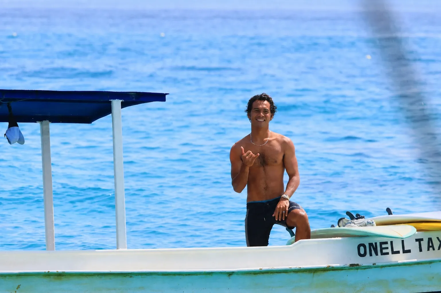 Loxy smiling and throwing a shaka on the Loxy Surf boat in the turquoise channel at Nusa Lembongan