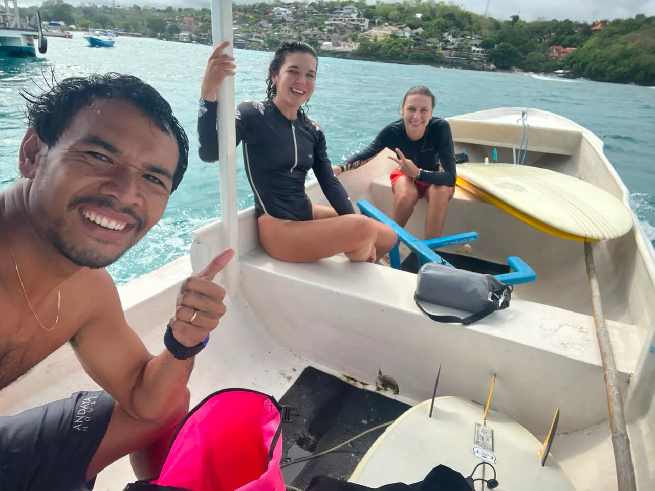 Loxy and two students riding the boat out to the break, surfboards loaded, Nusa Lembongan hillside behind