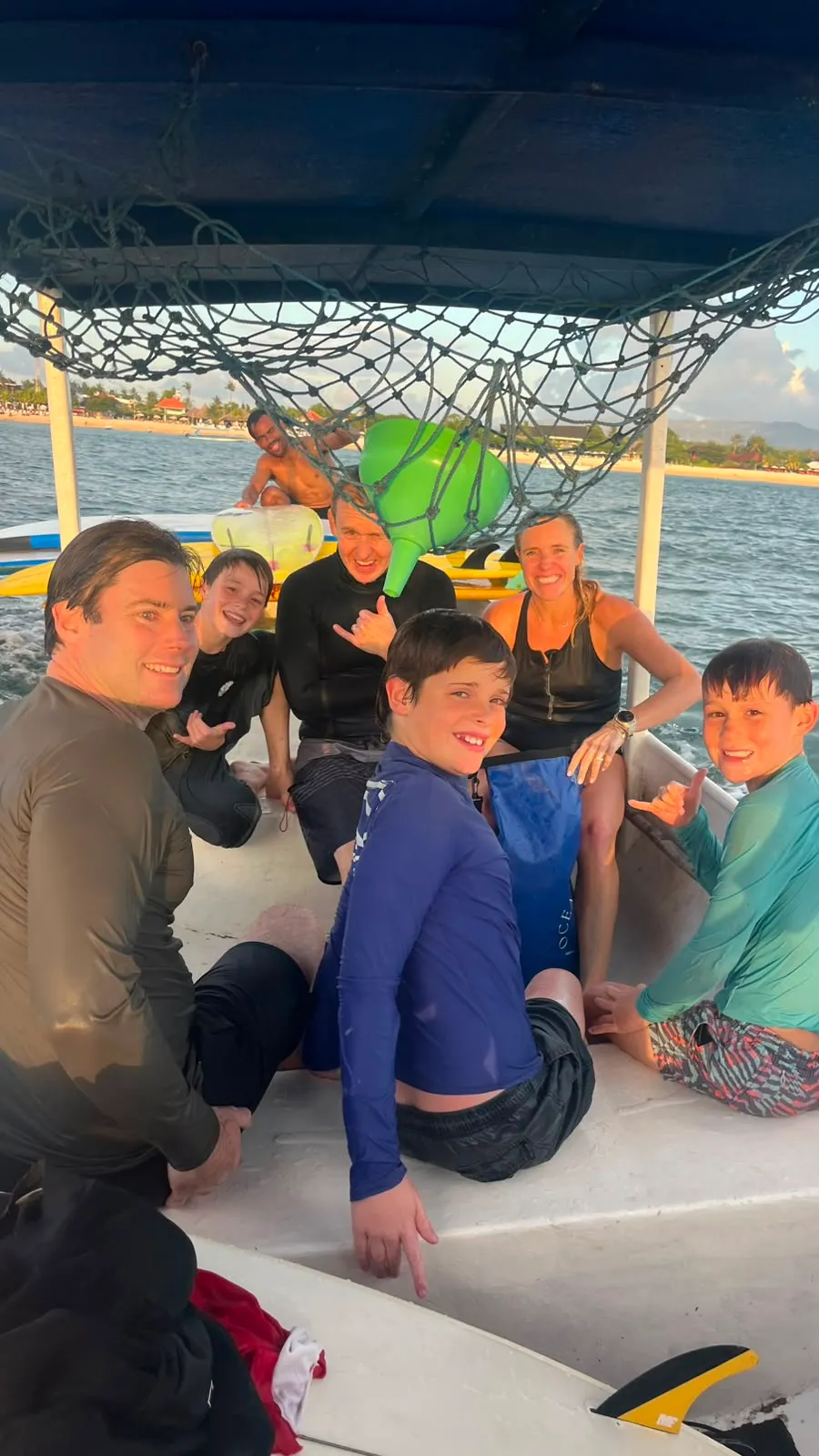 A happy family of surf students throwing shakas on the boat after a session at Nusa Lembongan, an instructor loading a board behind them