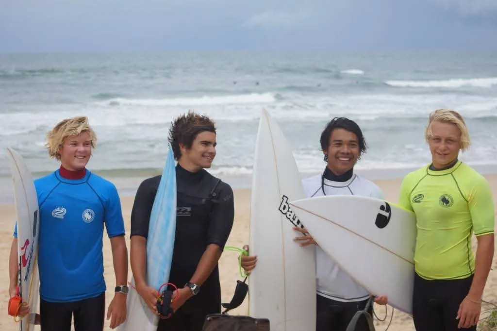 Loxy with three fellow junior surfers on the beach, boards under their arms, before a school surfing contest